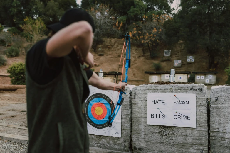 a man holding a bow and aiming at a target, pexels contest winner, excessivism, graffiti throws, king of the hill, subject action : holding sign, the cure for hate