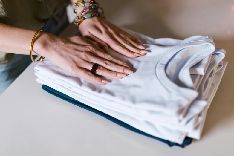 a woman holding a stack of clothes on top of a table, a silk screen, trending on unsplash, private press, wearing white shirt, close up details, partially cupping her hands, wearing a vest top