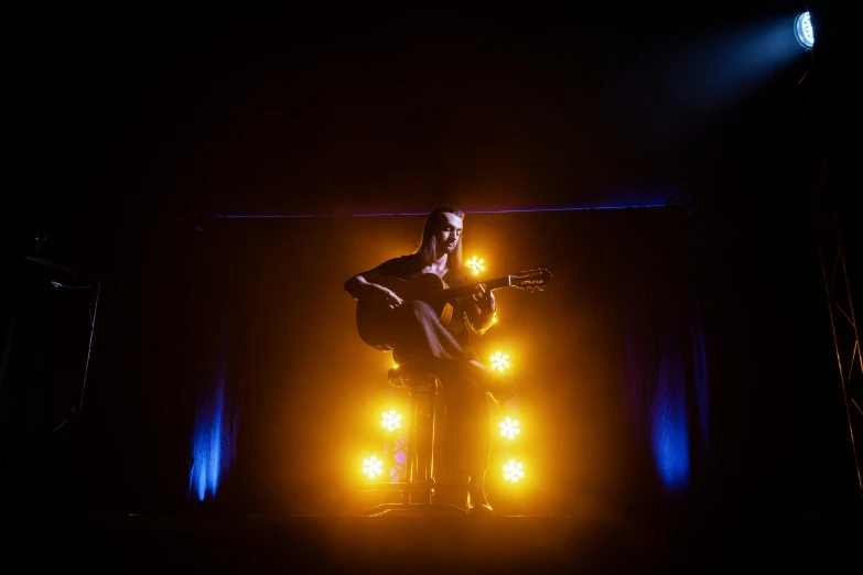 a man standing on top of a stage holding a guitar, aurora aksnes, ( ( stage lights ) ), colour photograph, sittin