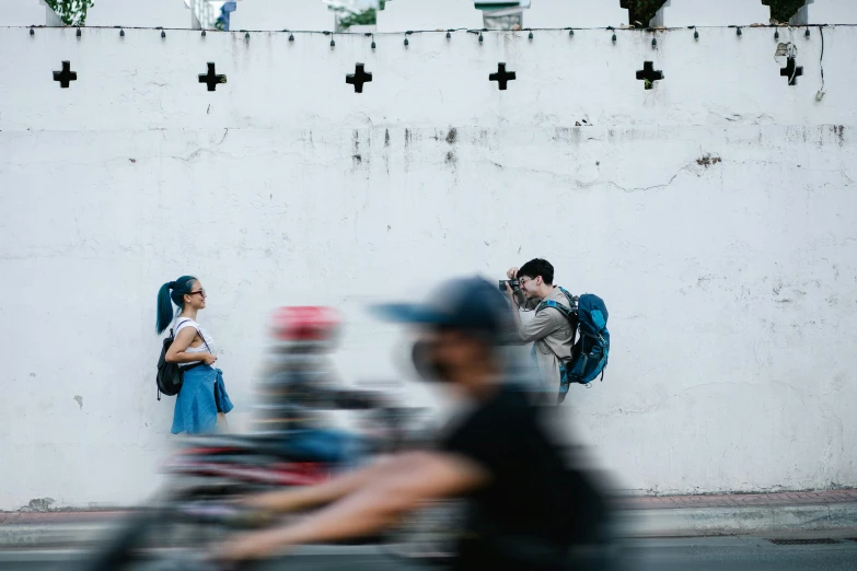 a man riding a bike down a street next to a wall, a picture, by Alejandro Obregón, unsplash contest winner, man and woman walking together, zoom blur, embracing, panoramic view of girl