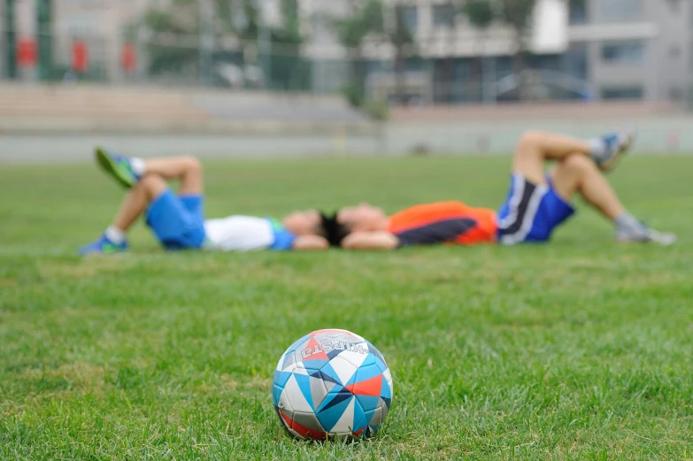 a soccer ball sitting on top of a lush green field, people resting on the grass, changquan, school class, sweaty