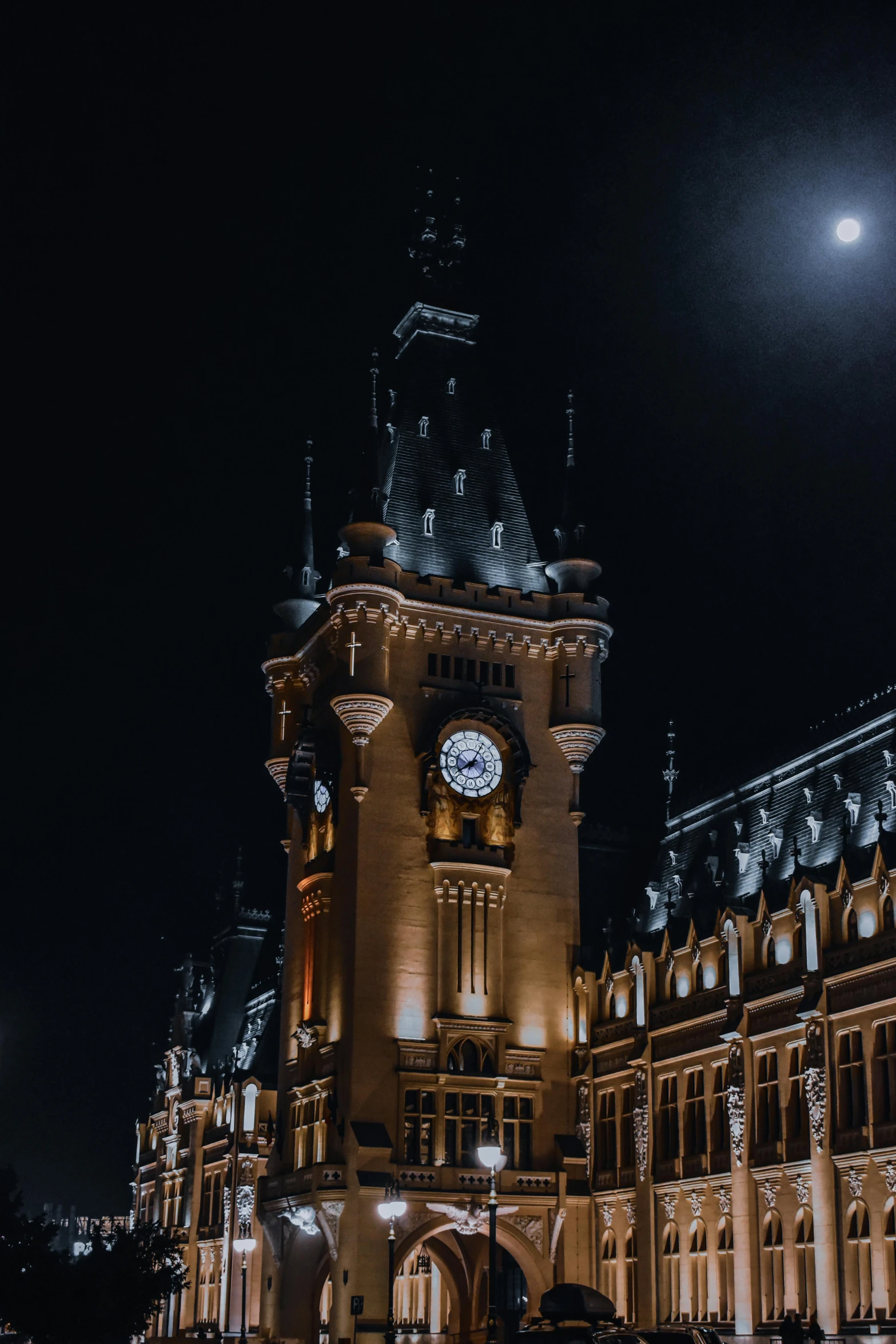 a large building with a clock tower lit up at night, by Adam Marczyński, train station, profile image, gothic revival, with the moon out