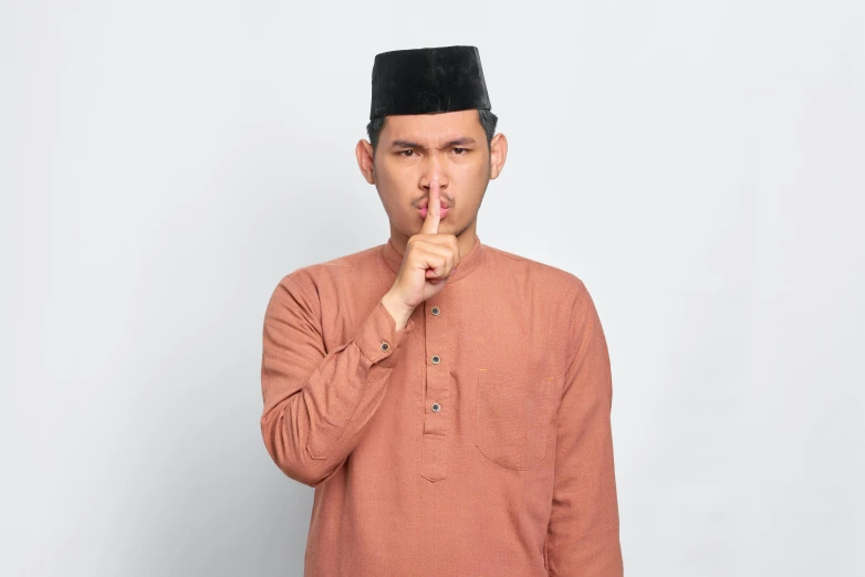 a man making a quiet gesture with his finger, by Basuki Abdullah, shutterstock, hurufiyya, wearing a brown, secret <, square nose, high quality image