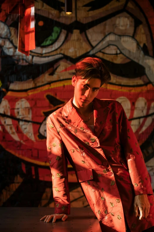 a man standing in front of a wall covered in graffiti, an album cover, red kimono, male model, joel fletcher, evening lighting