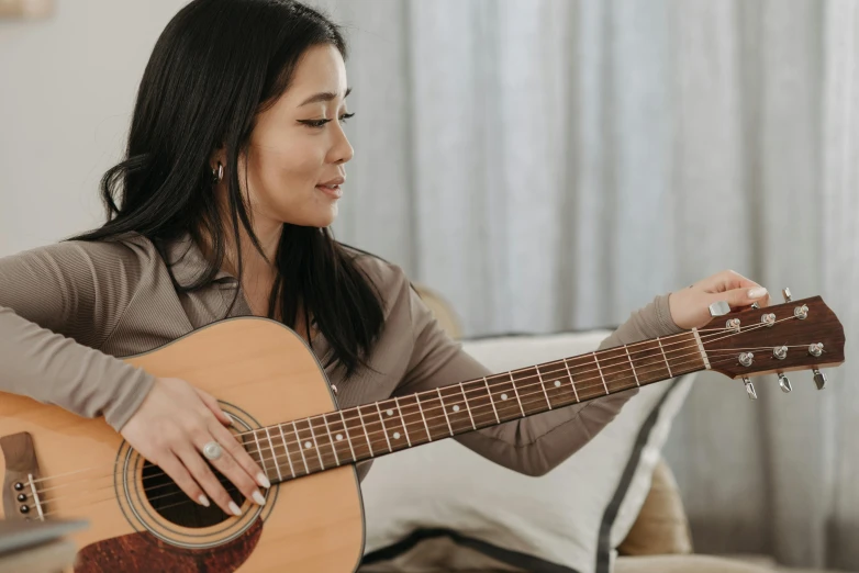 a woman sitting on a couch playing a guitar, inspired by Kawai Gyokudō, trending on pexels, shin hanga, right hand side profile, brown, detailed expression, ross tan