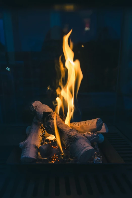 a close up of a fire on a grill, an album cover, by Robbie Trevino, pexels contest winner, renaissance, cozy night fireflies, lounge background, blue fire, a wooden