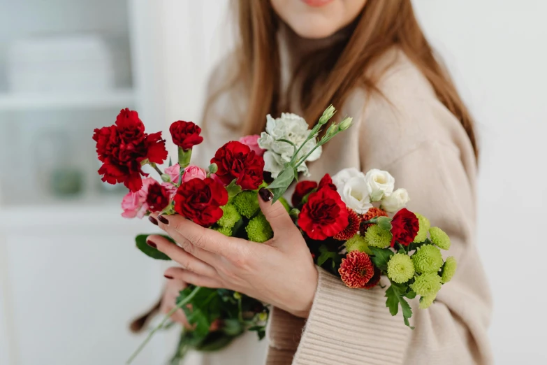 a woman holding a bunch of flowers in her hands, a still life, pexels contest winner, red and white, wearing a scarlet hoodie, subtle detailing, flirty