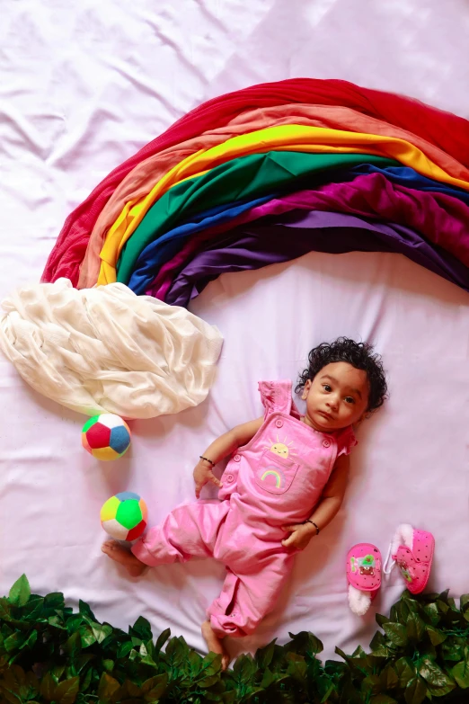 a baby laying on top of a bed next to a rainbow, process art, indian girl with brown skin, full body picture, 2019 trending photo, photo on iphone