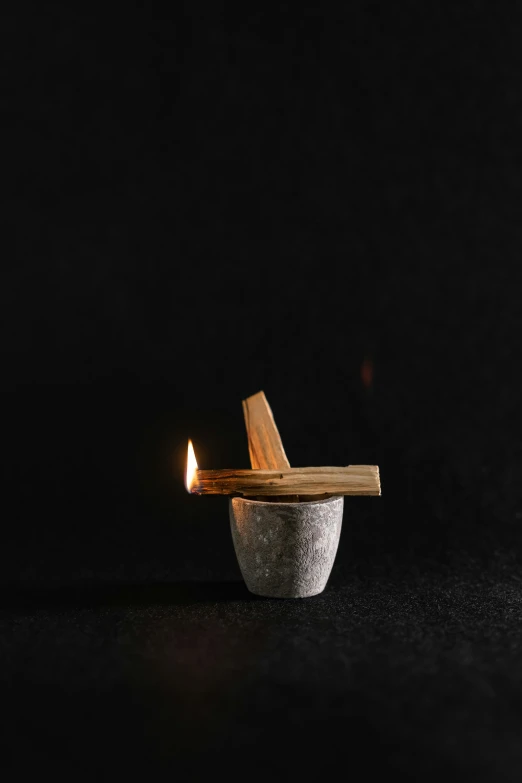 a candle with a wooden stick sticking out of it, an abstract sculpture, inspired by Kaigetsudō Ando, unsplash, tiny smokes from buildings, mortar and pestle, on black background, dwell