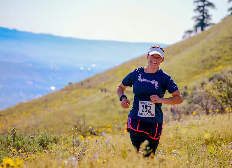 a woman running on a trail with mountains in the background, in a race competition, rowena morrill, 2 0 2 2 photo, flowers