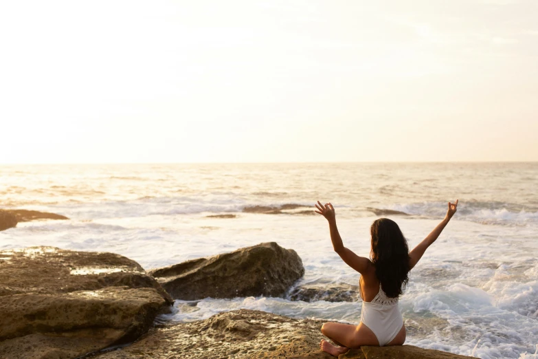 a woman sitting on top of a rock next to the ocean, ajna chakra, waving arms, profile image, warm glow