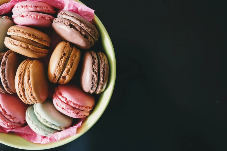 a bowl filled with macarons sitting on top of a table, a colorized photo, pexels contest winner, thumbnail, cookies, brown and magenta color scheme, pink white and green