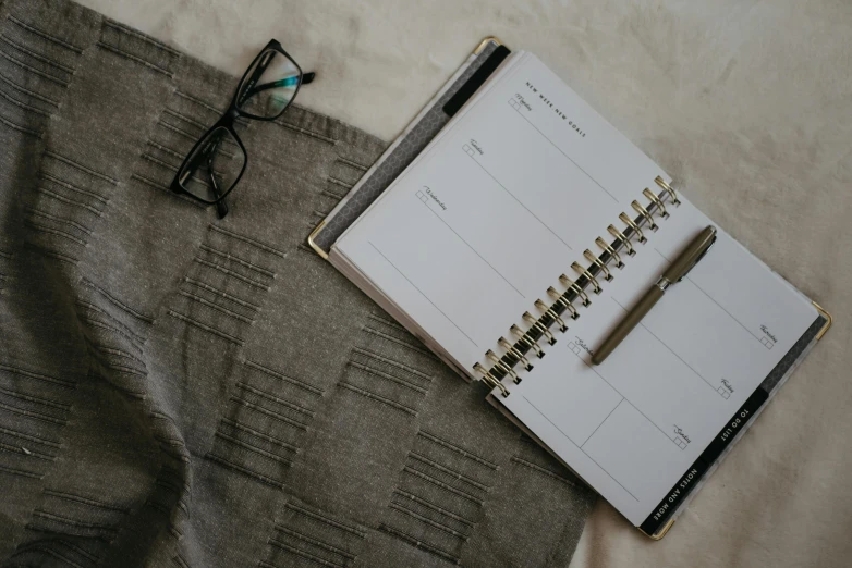 a notepad sitting on top of a bed next to a pair of glasses, trending on pexels, minimalism, grey clothes, patterned, female calendar, bird's eye