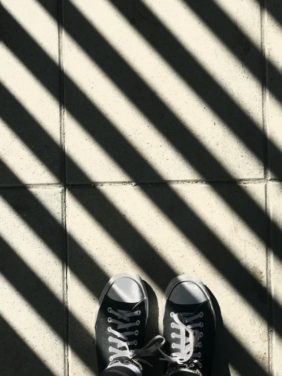 a pair of black sneakers sitting on top of a tiled floor, rays of sunshine, black stripes, captured on iphone, vertical lines