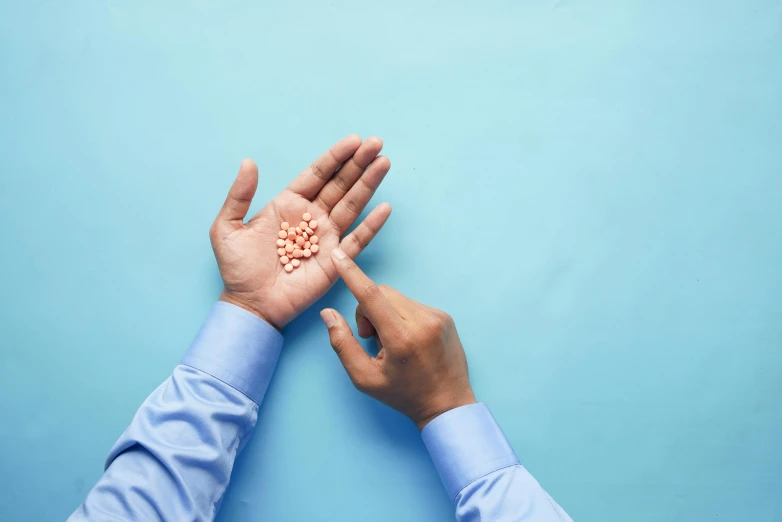 a man holding a handful of cereal in his hands on a blue background, an album cover, by Gavin Hamilton, pexels, plasticien, pills and medicine, hand on table, (doctor), made of nanomaterials