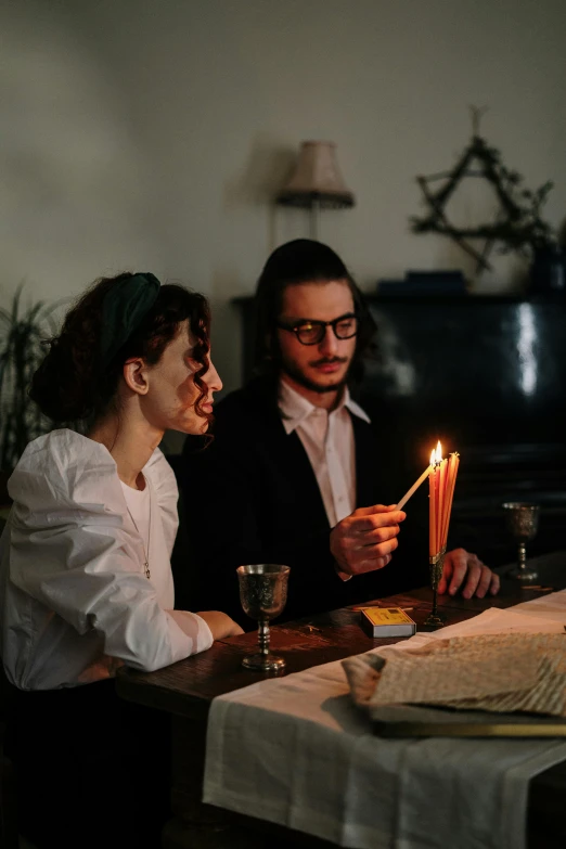 a man and a woman sitting at a table with a lit candle, jewish young man with glasses, 2019 trending photo, spell casting, gif