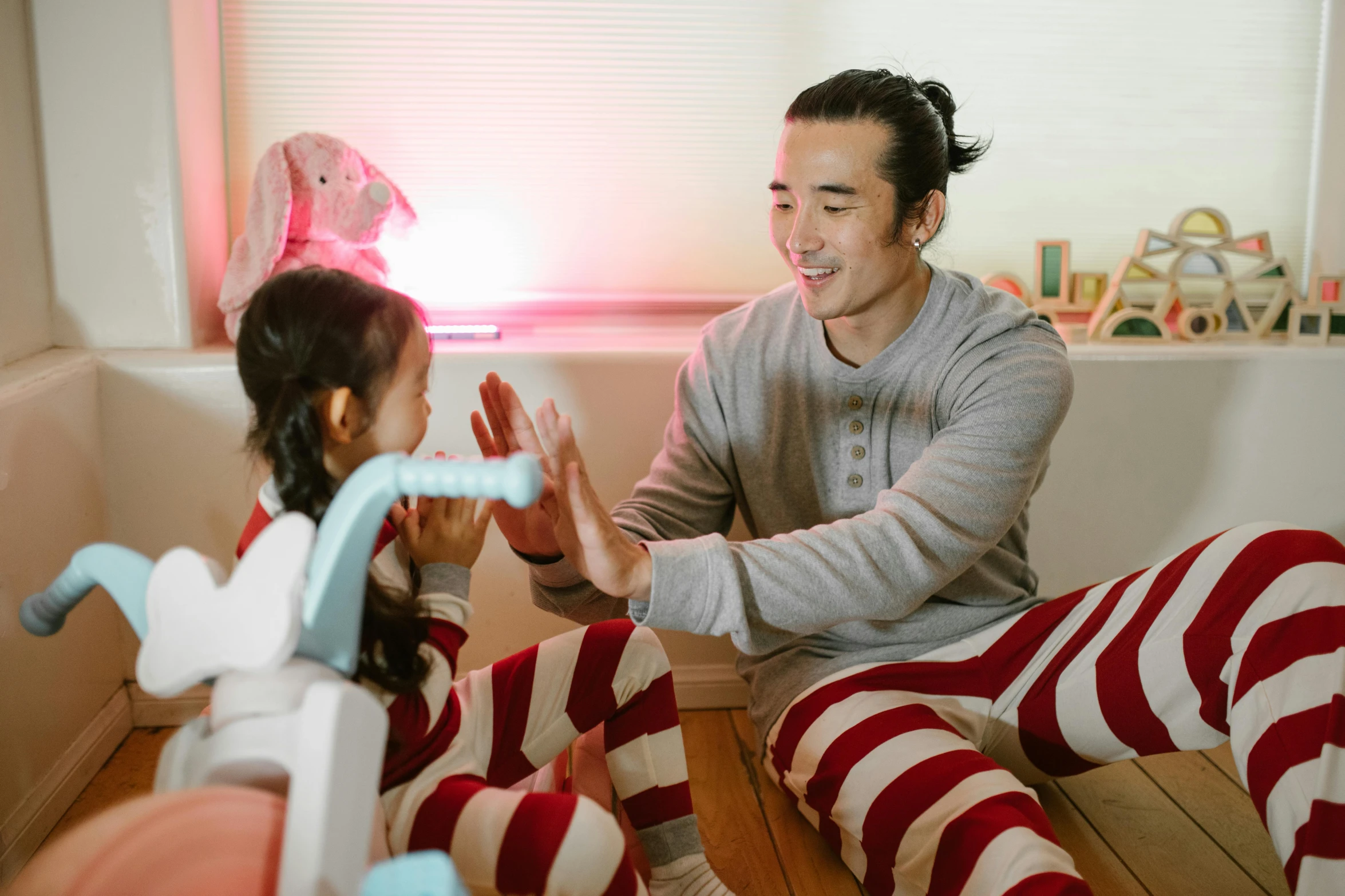 a man sitting on top of a wooden floor next to a little girl, wearing pajamas, avatar image, david luong, smiling playfully