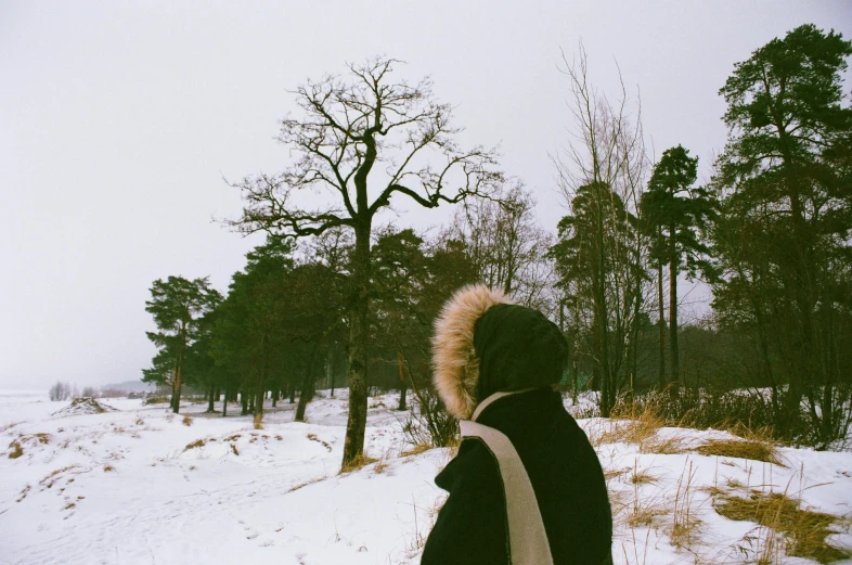 a person that is standing in the snow, an album cover, by Christen Dalsgaard, pexels contest winner, visual art, trees in background, looking sideway, vintage aesthetic, wearing black coat
