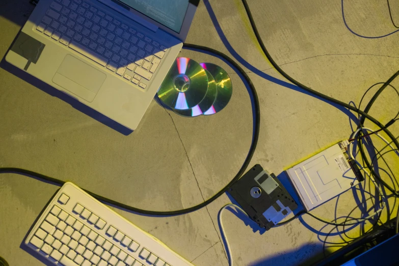 a laptop computer sitting on top of a table next to a cd, computer art, cables on floor, collaboration, cyber aesthetic, overview