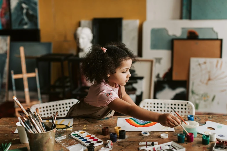 a little girl sitting at a table painting, pexels contest winner, future activist, trending on artsation, painting on a badge, wooden art toys