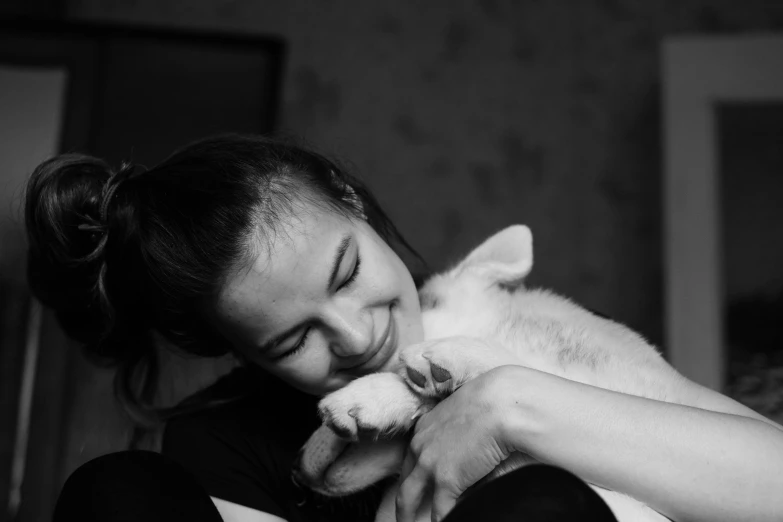 a black and white photo of a woman holding a cat, by Emma Andijewska, pexels contest winner, romanticism, puppies, happy cozy feelings, fennec, teenage girl