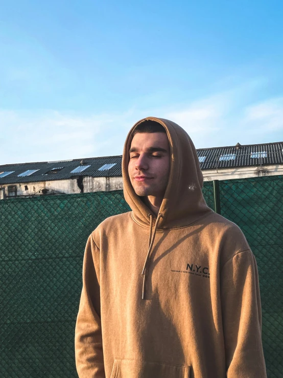 a man standing on top of a tennis court holding a racquet, an album cover, by Niko Henrichon, unsplash, lyco art, beige hoodie, ((portrait)), oversized hoodie, wearing a brown