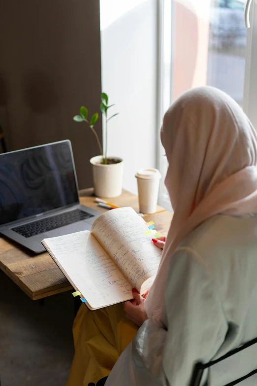 a woman sitting at a table in front of a laptop computer, hurufiyya, an open book, profile image, islamic, multiple stories