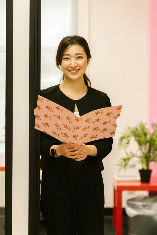 a woman standing in front of a mirror holding a piece of paper, an album cover, unsplash, shin hanga, in the office, wearing pink floral chiton, wearing business casual dress, ethnicity : japanese