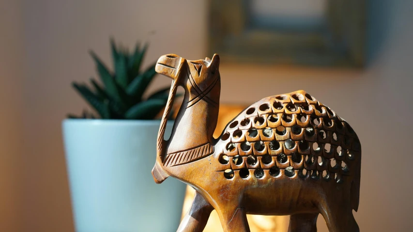 a wooden figurine of a camel next to a potted plant, by John Henderson, unsplash, folk art, patterned, bronze skinned, warm light, close up shot from the side