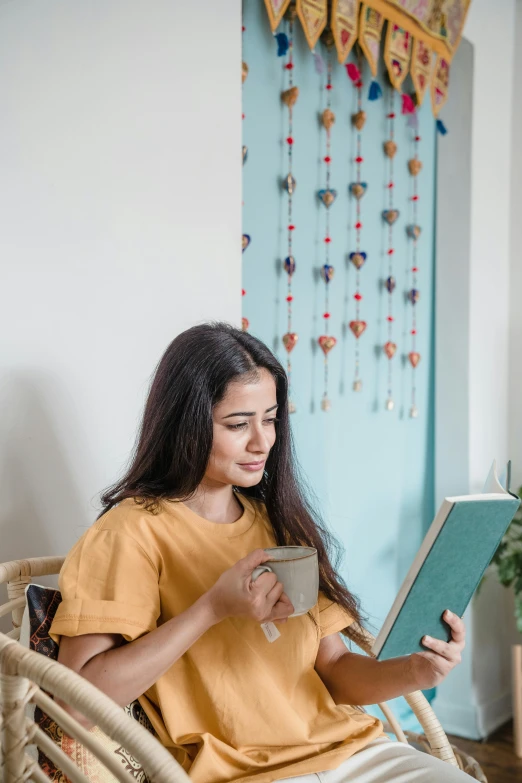 a woman sitting in a chair reading a book, pexels contest winner, hurufiyya, wearing a modern yellow tshirt, assamese aesthetic, with teal clothes, profile image