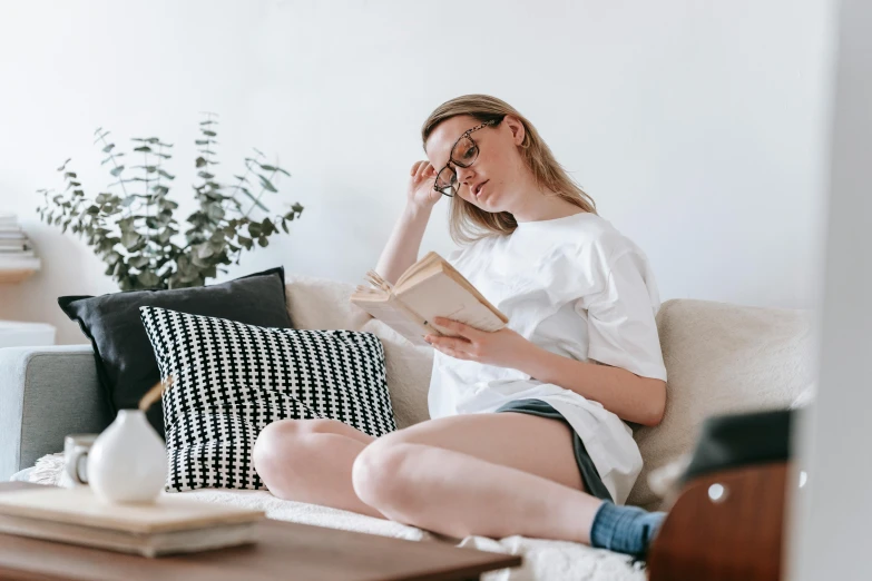 a woman sitting on a couch reading a book, pexels contest winner, figuration libre, dressed in a white t shirt, pregnant, nerdy appearance, pale skin