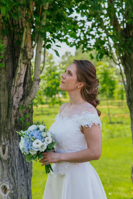a woman in a wedding dress standing next to a tree, sky blue and white color scheme, medium head to shoulder shot, bouquets, over-the-shoulder shot