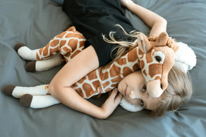 a little girl laying on a bed with a stuffed giraffe, inspired by Sarah Lucas, pexels contest winner, hurufiyya, hugging each other, high angle, looking sad, long neck