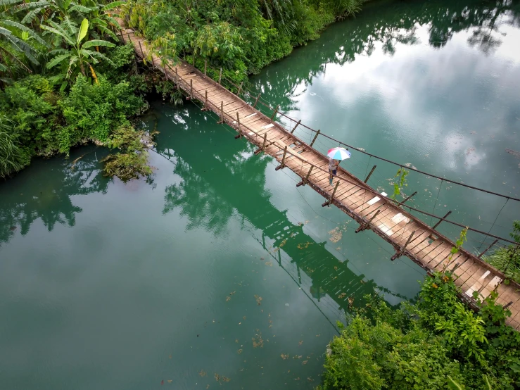 a person walking across a wooden bridge over a river, inspired by Steve McCurry, pexels contest winner, hurufiyya, jamaica, avatar image, aerial, vietnam