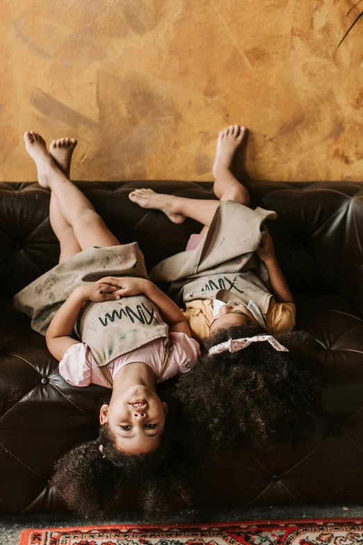 a couple of kids laying on top of a couch, pexels contest winner, beautiful gemini twins, brown and cream color scheme, black teenage girl, leather robes