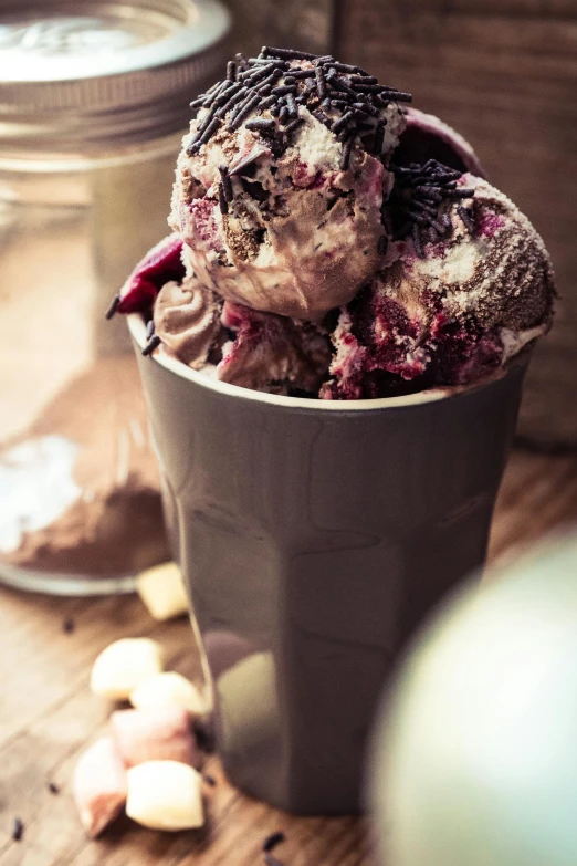a cup of ice cream sitting on top of a wooden table, dark purple scheme, gooey skin, milkshake, seeds