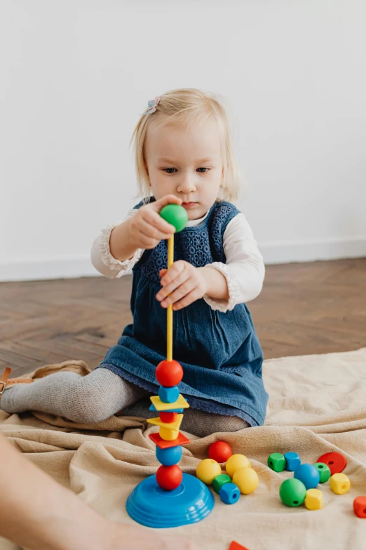 a little girl sitting on the floor playing with a toy, inspired by Constantin Hansen, pexels contest winner, tall towers, embedded with gemstones, premium quality, holding a wooden staff