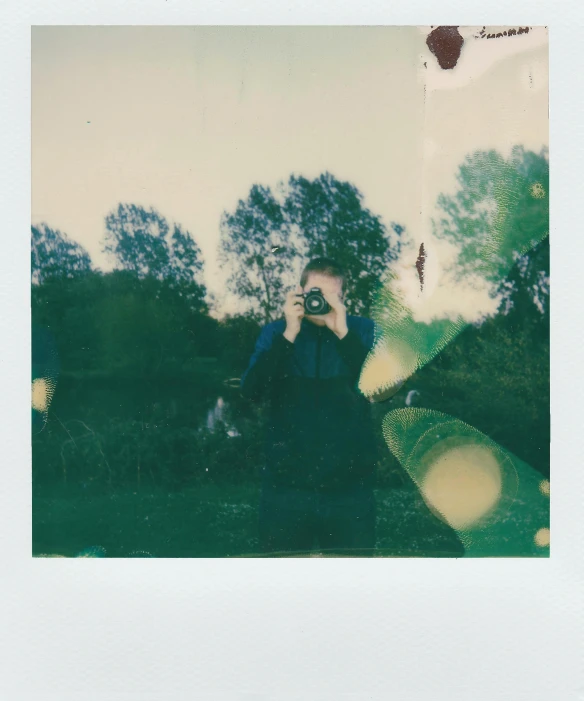 a person taking a picture with a camera, a polaroid photo, inspired by Elsa Bleda, happening, in a open green field, slightly holographic, scanned in, on a pale background