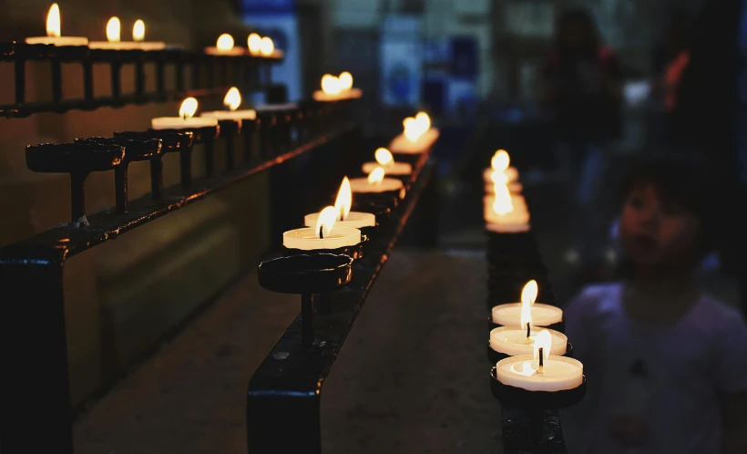 a row of lit candles in a church, by Niko Henrichon, pexels, mourning, instagram post, panels, over the shoulder