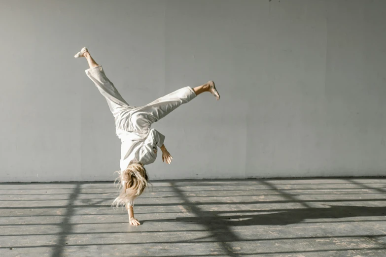 a person doing a handstand in a room, arabesque, grey, background image, a blond, wearing a track suit