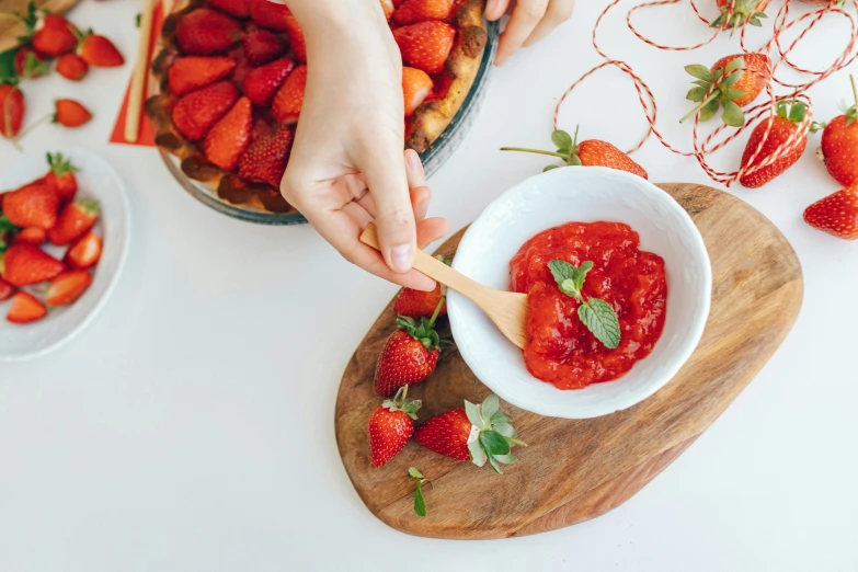 a person holding a wooden spoon over a bowl of strawberries, by Emma Andijewska, pexels contest winner, tomato sauce, on a white table, desserts, product introduction photo