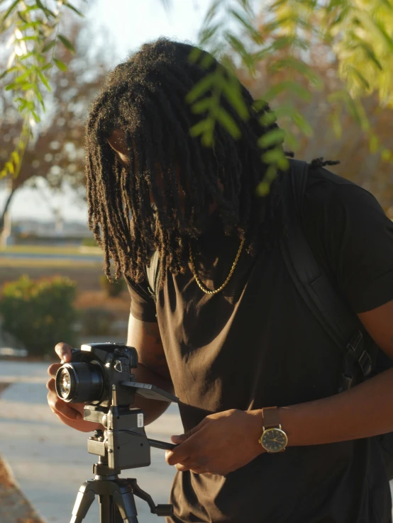 a man standing next to a camera on a tripod, unsplash, video art, dreadlock black hair, low quality footage, a black man with long curly hair, ( ( theatrical ) )