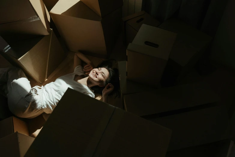 a woman laying on the floor surrounded by boxes, by Emma Andijewska, pexels contest winner, light and space, laughing, avatar image, standing in a dimly lit room, movies