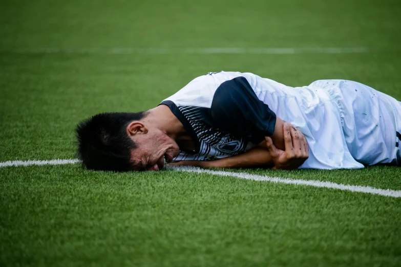 a man laying on top of a soccer field, by Julia Pishtar, pexels contest winner, crying and puking, asian male, medical, side view of a gaunt