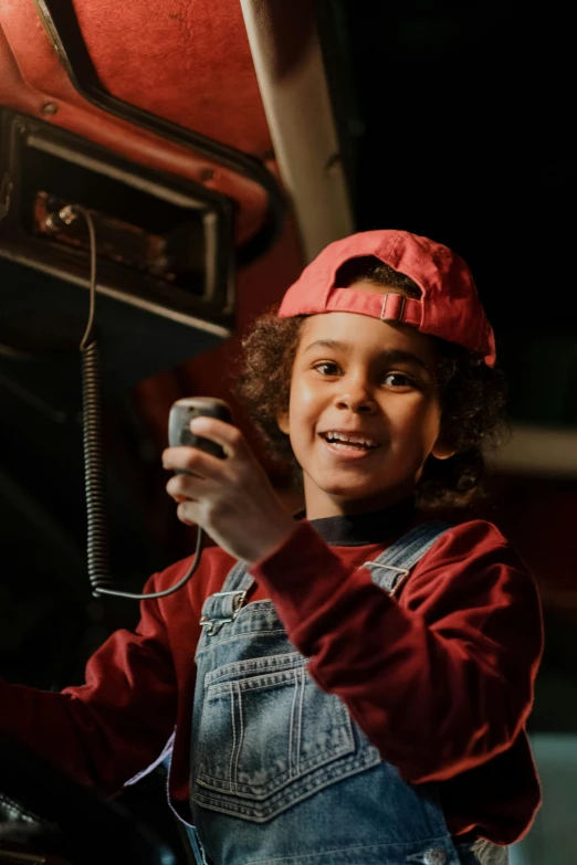 a close up of a person holding a cell phone, the electric boy, red hat, taking control while smiling, for junior