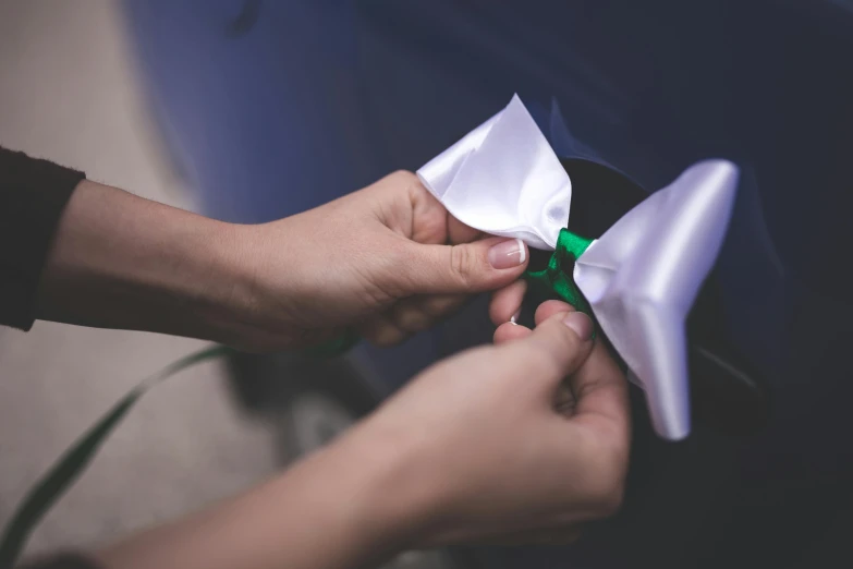 a person cutting a piece of paper with a pair of scissors, a colorized photo, by Adam Marczyński, unsplash, happening, bowknot, takata yamamoto style, green and white, satin ribbons