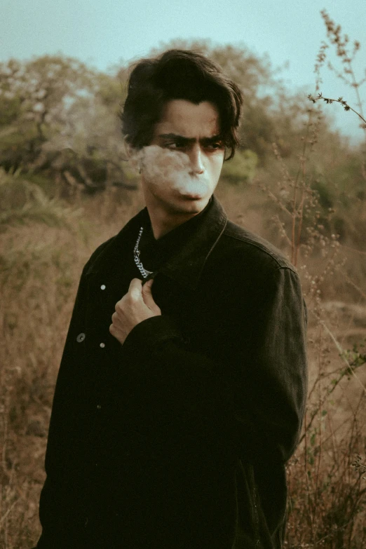 a man standing in a field with a cigarette in his mouth, an album cover, pexels contest winner, avan jogia angel, profile picture, spooky photo, cheekbones