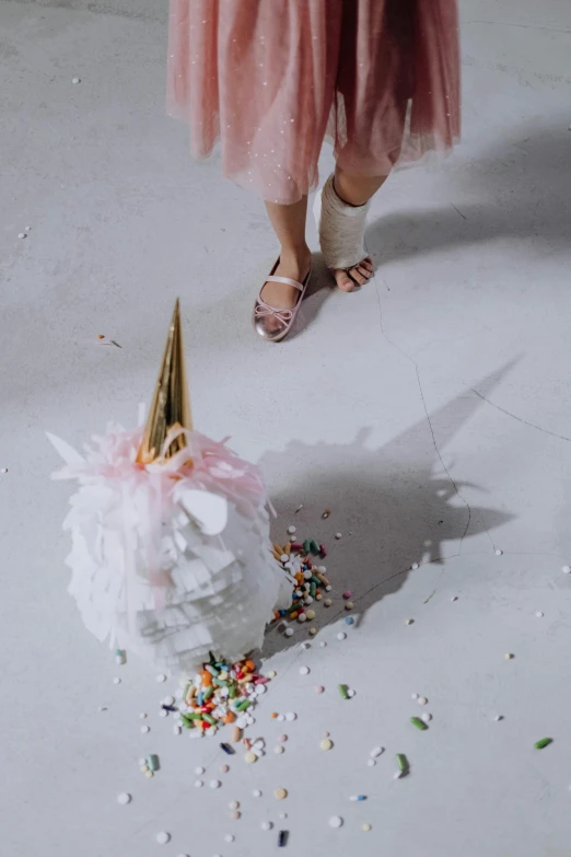 a woman in a pink dress standing next to a unicorn pom pom, trending on unsplash, birthday cake on the ground, bird's view, on a white table, foil