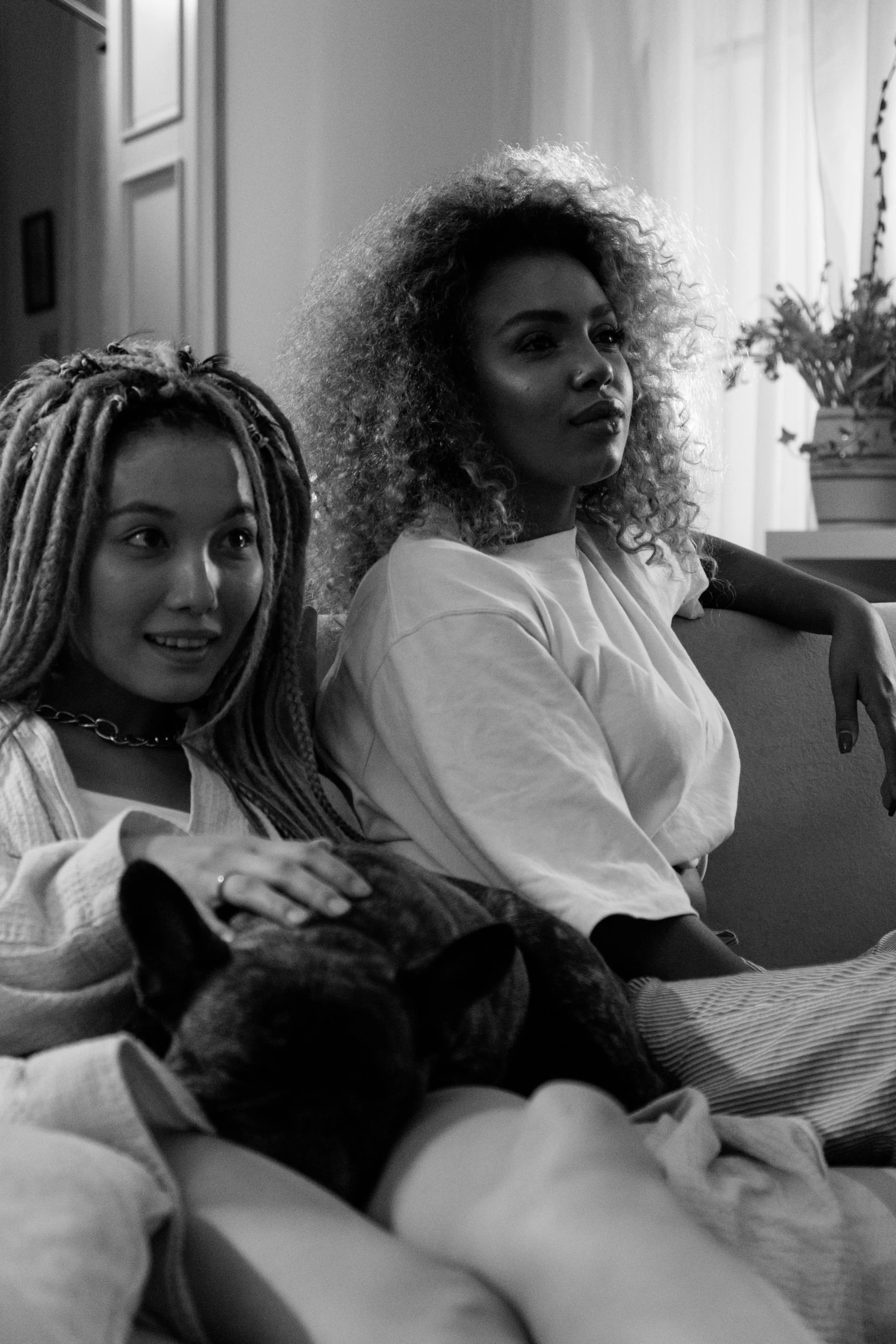 a couple of women sitting on top of a couch, a black and white photo, by Sophia Beale, pexels, antipodeans, doja cat, wearing white pajamas, braids, official music video