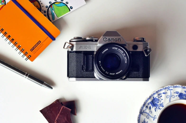 a camera sitting on top of a table next to a cup of coffee, inspired by Henri Cartier-Bresson, unsplash contest winner, photorealism, caramel, colorful pentax camera, on a white table, canon a1